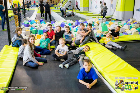 Baner: dzieci siedzą i leżą na trampolinach. w głębi miękkie kostki z pianki.