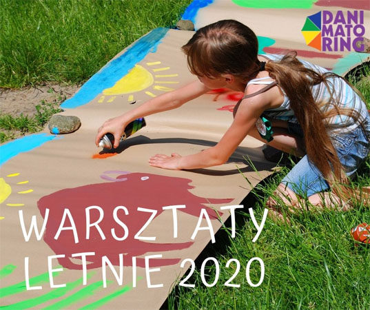 Dziwczyna maluje słońce i zwierzęta na szrym papierze rozłozonym na trawie.