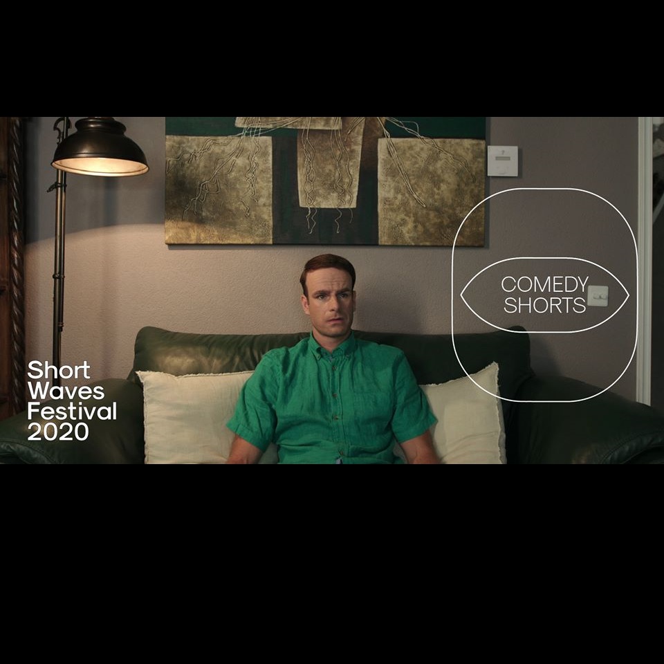 Kadr obrazu na którym widzimy mężczyznę w zielonej koszuli z krótkim rękawem, siedzącego na zielonej dwuosobowej kanapie z dwoma białymi poduszkami za plecami. W tle również lampa stojąca, zaświecona oraz fragment obrazu nad kanapą. Na kadr nałożono logo festiwalu oraz cyklu comedy shorts.