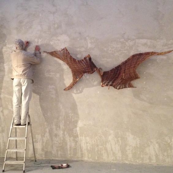 Zdjęcie artysty wieszającego swoją pracę na ścianie galerii.