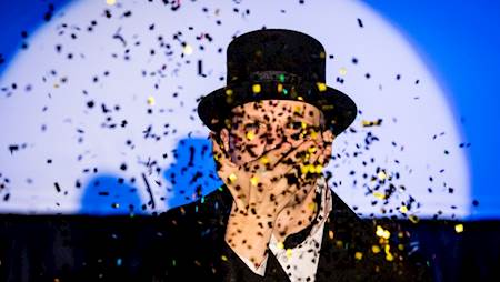 Fotografia mężczyzny w cylindrze a przed nim padające konfetti.