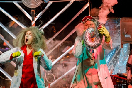 Na zdjęciu widać dwoje naukowców, kobietę i mężczyznę o siwych, bujnych włosach. Bohaterka Nielemka ubrana jest w czerwony kombinezon oraz biały fartuch opatrzony różnymi wzorami chemicznymi i matematycznymi. Bohater Lemtak ma widoczne na czole okulary i dmucha w rurę wentylacyjną, z której wylatuje dym.