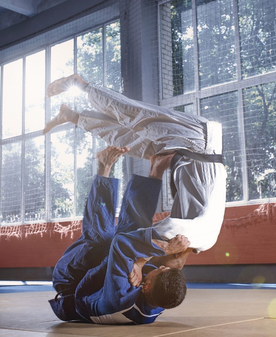 Dwóch zawodników ubranych w białą i niebieską judogę ćwiczy judo.