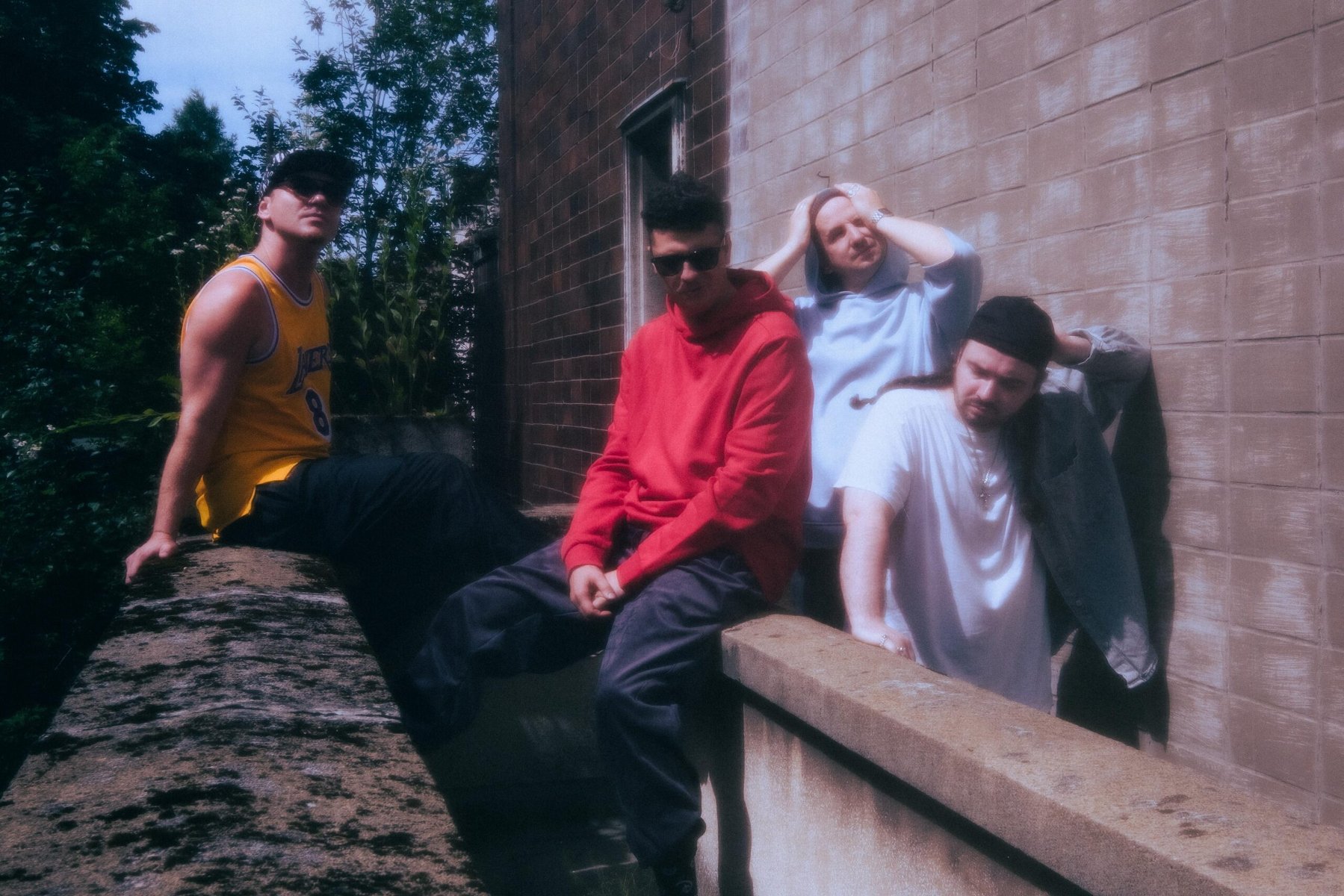 Czterech mężczyzn siedzi i stoi przy murku obok ściany budynku.