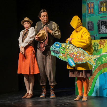 Bohaterowie, Dora Dynks i Waldemar Wihajster, stoją wyraźnie wstrząśnięci obok postaci w żółtej kurtce przeciwdeszczowej i pomarańczowych rajstopach, któa niesie wielką, wyszczerzoną, rysunkową rybę.