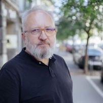 Brodaty mężczyzna w okularach stoi na ulicy.