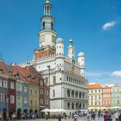 Budynek ratusza widziany od strony głównego wejścia. Jest lato, niebo jest błękitne, a po płycie Starego Rynku spacerują ludzie.