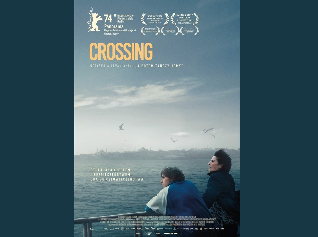 Plakat przedstawia dwie osoby, starszą kobietę i nastolatka, stojących przy barierce, z której obserwują morze. Są zadumani.