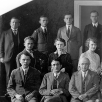 Czarno-białe zdjęcie grupowe elegencko ubranych kobiet i mężczyzn. Część grupy stoi, część siedzi.