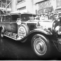 Czarno-białe zdjęcie starego samochodu. Dookoła pojazdu tłumy gapiów.