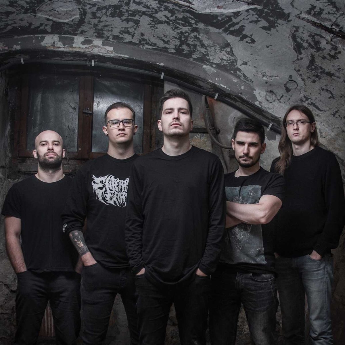 Zdjęcie pięciu mężczyzn w czarnych koszulkach, którzy stoją na tle odrapanej ściany.