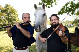 Dwóch mężczyzn grających na instrumentach i stojący pomiędzy nimi biały koń.