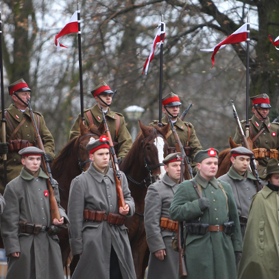 Dwa rzędy umundurowanych powstańców (grupa rekonstrukcyjna), podczas obchodów powstania wielopolskiego. Z przodu stoją zbronią na ramieniu, z tłu są na koniach.