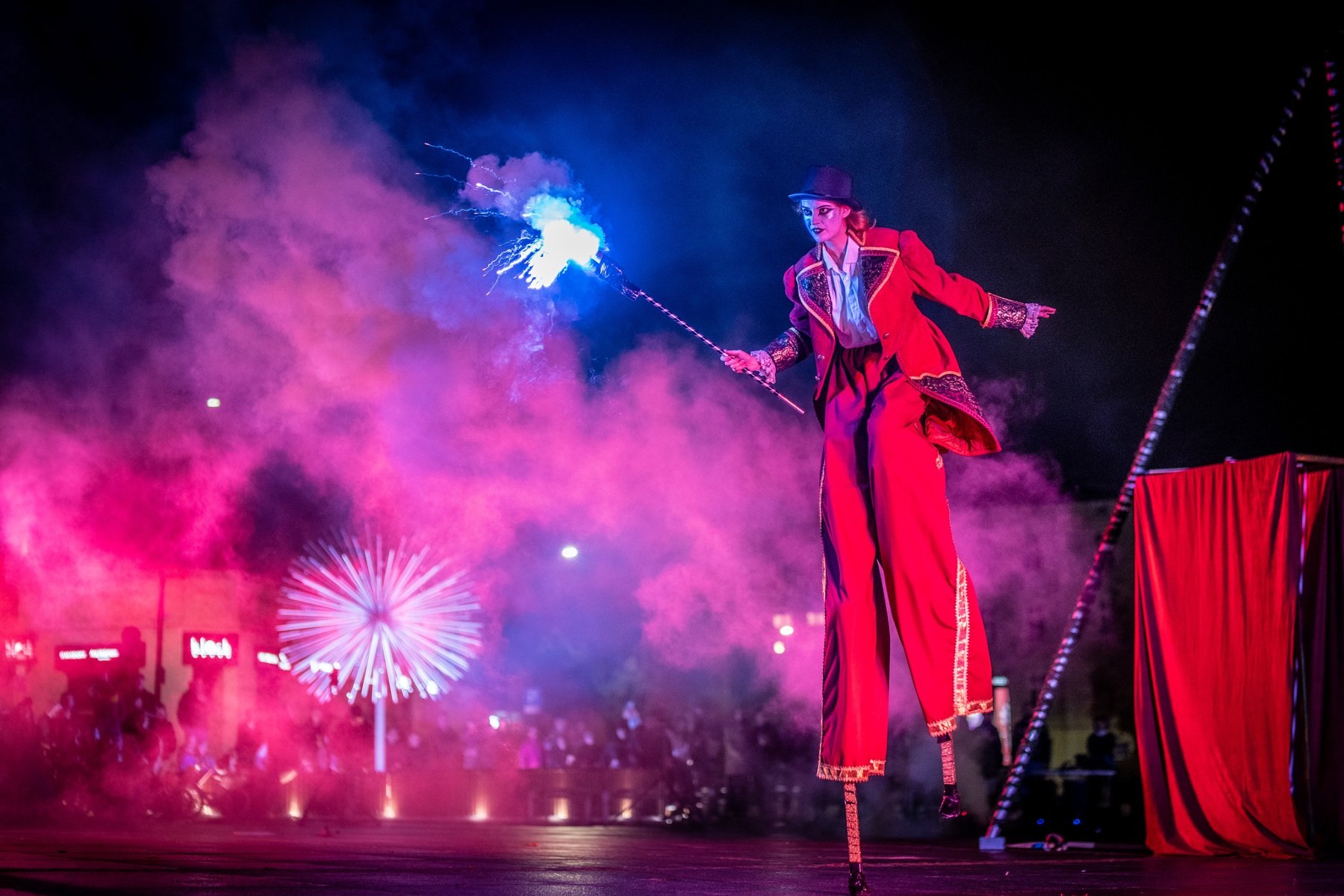 Aktorka na szczudłach w ręku trzymająca sztuczne ognie.