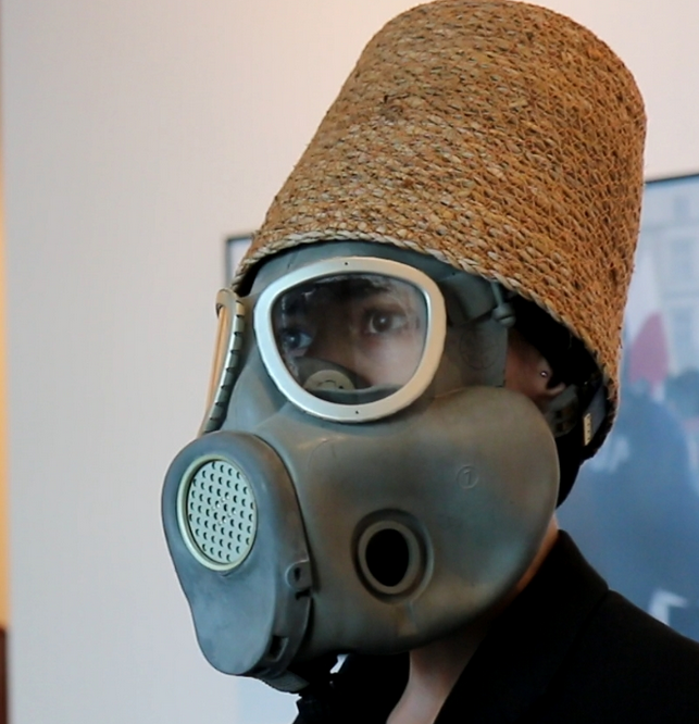 Mężczyzna w masce gazowej i wiklinowym koszu na głowie.