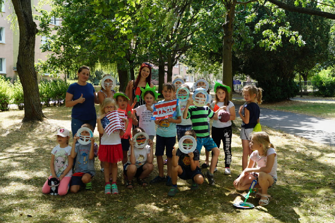 Dzieci z opiekunką podczas półkolonii, trzymające gadżety.