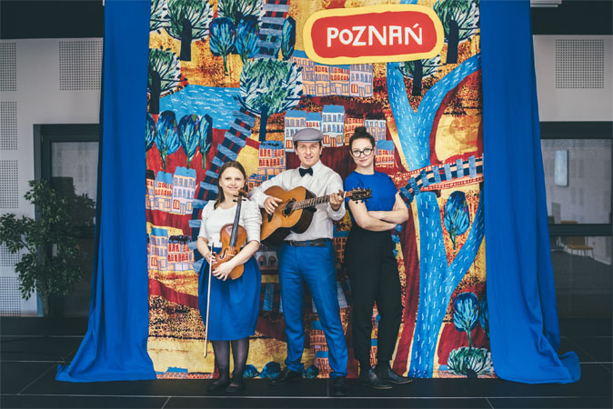 Artyści: 2 kobiety i mężczyzna, na tle rysunków Poznania.