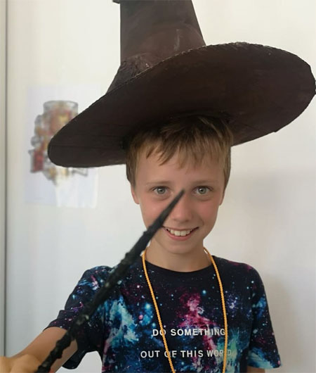 Uśmiechnięty chłopiec w kapeluszu czarodzieja z różdżką w dłoni.