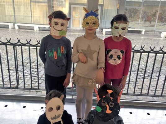 % dzieci w maskach z papieru. 3 stoi, 2 kuca.