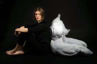 Krystyna Lipka-Czajkowska siedzi na podłodze, ręce położyła na kolanach, oparta o uszytą rzeźbę kobiety ułożonej w podobnej pozycji.