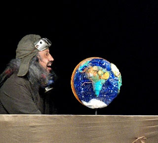 Mężczyzna w kurtce, szaliku, czapce-pilotce i goglach patrzy na globus.