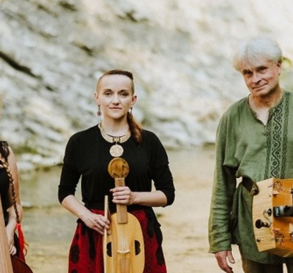 Fotografia ukazuje troje muzyków, dwie kobiety oraz mężczyznę, w tle znajduje się skaliste wzgórze. Cała trójka stoi przed aparatem trzymając instrumenty muzyczne, viola da gamba, vielle oraz lirę korbową. Łagodnie się uśmiechają.