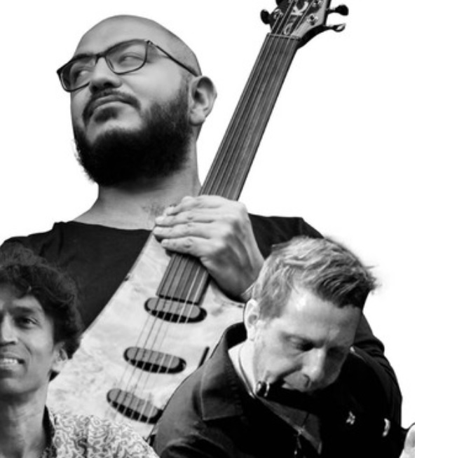 Grafika to kolaż czarno-białych portretów trzech muzyków. Jeden z nich trzyma gitarę, drugi gra na flecie poprzecznym, trzeci - na tabli.