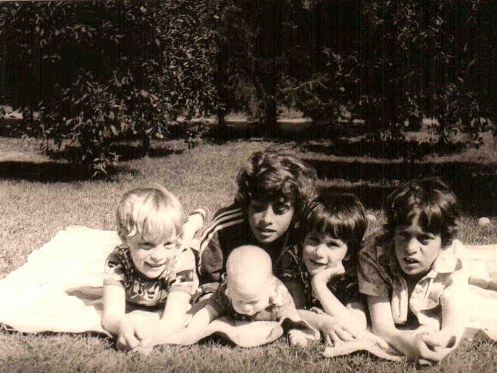 Fotografia przedstawiająca pięcioro dzieci leżące na kocu w sadzie.