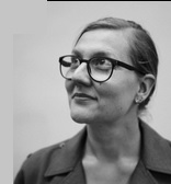 Na zdjęciu jest Marta Madejska, w portretowym ujęciu. Ma związane, gładko zaczesane włosy, okulary w wyrazistych oprawkach i marynarkę. Jej głowa skierowana jest w lewo, patrzy w górę z delikatnym uśmiechem.