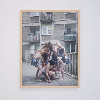 Fotografia na ścianie galerii przedstawiająca grupę ludzi na tle szarego blokowiska.