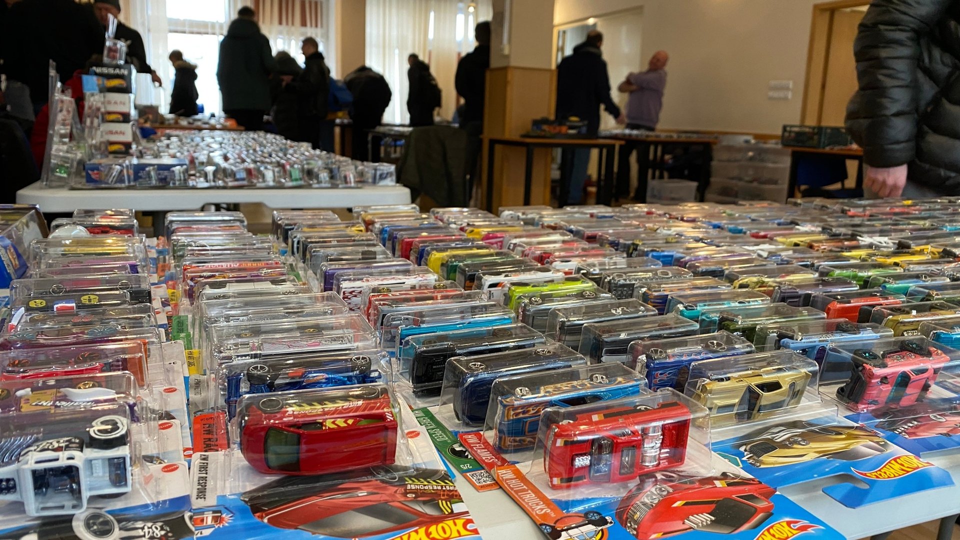 Na stolikach rozłożone samochodziki zabakowe marki Hotwheels. Między stolikami chodzą kupujący.