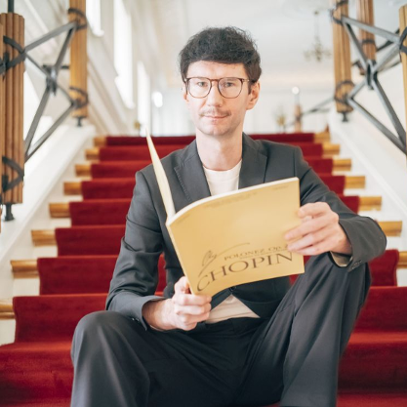 Jakub Dera siedzi na schodach biblioteki, w rękach trzyma zeszyt nut podpisany "Chopin".