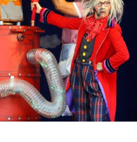 zdjęcie przedstawia postać w kolorowym stroju stojącą przy machinie przypominjącej rakietę