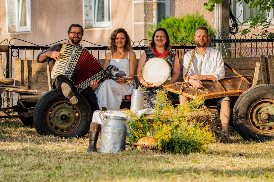 Cztery osoby z ludowymi instrumentami siedzą na drewnianej przyczepie.