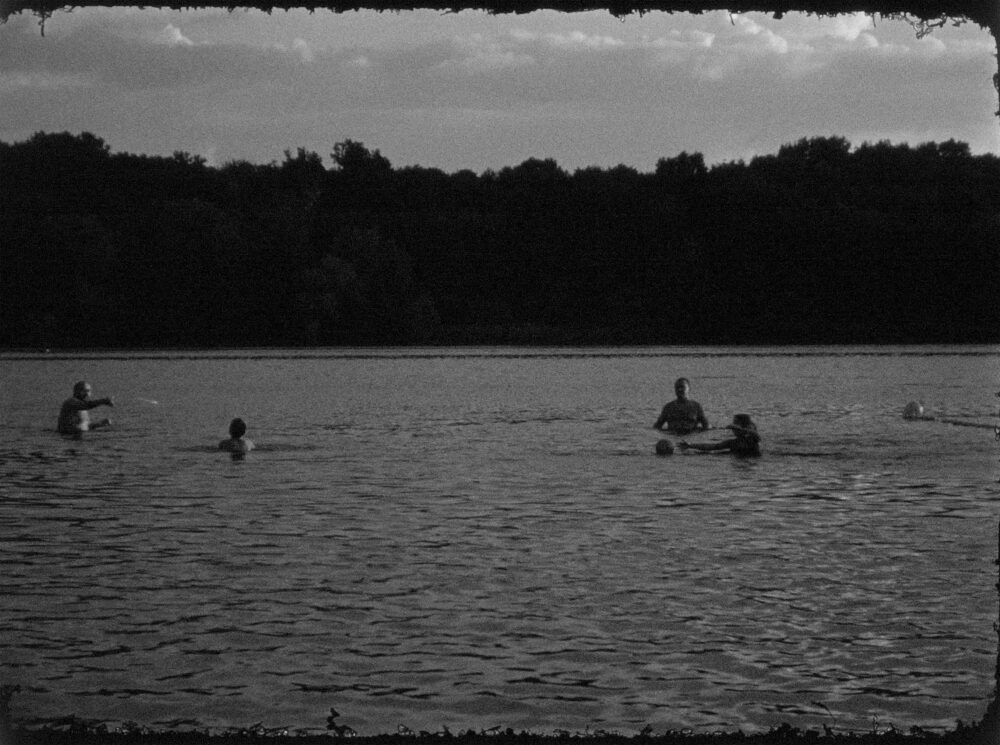 Czarno-biała fotografia kąpiących sie ludzi w jeziorze.
