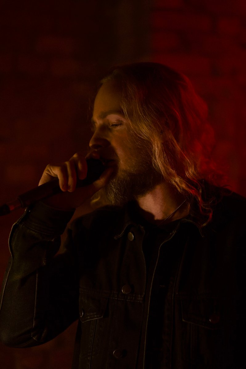 Na ciemnym tle osoba, która śpiewa do mikrofonu