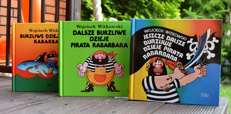 Trzy ksiązki stojące obok siebie z kolorowymi okładkami z piratem. W tle zielone drzewa.