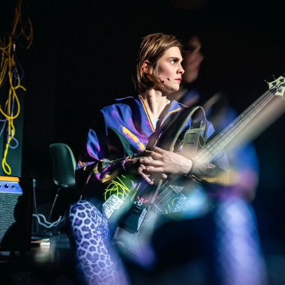 Kolorowo ubrana dziewczyna z gitarą na kolanach patrzy w bok.