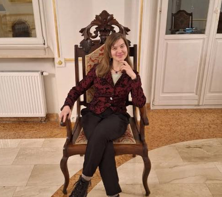 Zdjęcie artystki, która siedzi na drewnianym, tapicerowanym krześle.