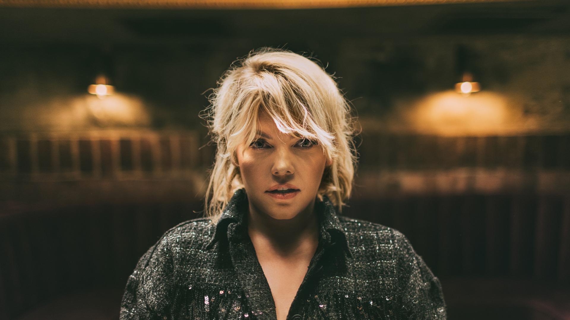 Zdjęcie Anny Dąbrowskiej od frontu. W tle rozmyte zaciemnione pomieszczenie.