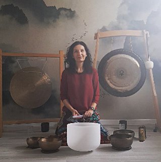 Kobieta nachyla się nad misą do grania, za nią stoją dwa gongi.