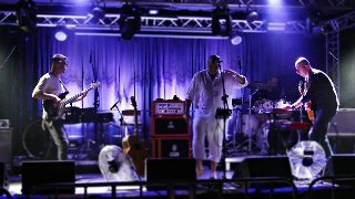 Zdjęcie przedstawia czterech muzyków rockowych występujących na scenie.