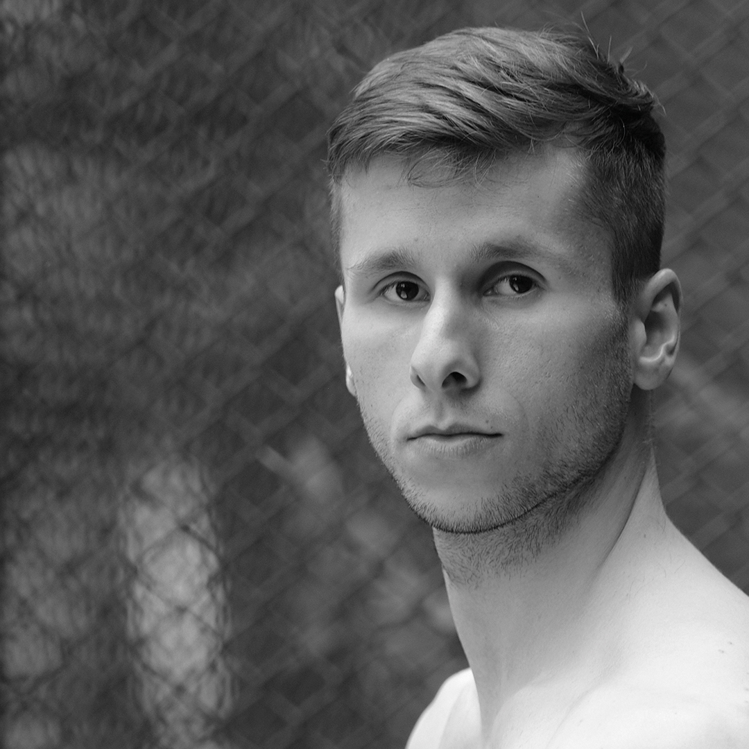 Czarno-białe zdjęcie przedstawia twarz tancerza Daniela Michny, patrzącego wprost w kierunku, z którego wykonano zdjęcie.