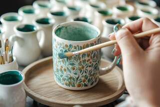 Ceramiczny kubek i malujący go pędzel.