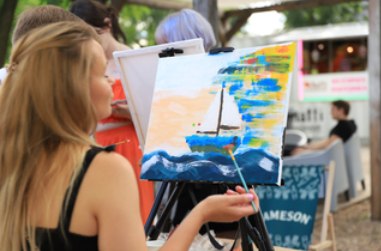 Osoba maluje obraz na sztaludze farbami akrylowymi.