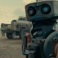 Metalowy robot z dwoma szkiełkami w miejscu oczu, za nim pustkowie i samochód.