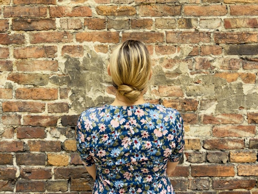 Kobieta stoi zwrócona przodem do ceglanej ściany.