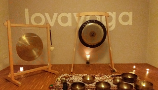 Zdjęcie przedstawia misy i gongi stojące pod ścianą, na której jest napisana nazwa miejsca koncertu na owe instrumenty, czyli Lovayoga.