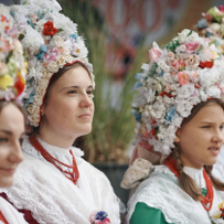 Młode kobiety w tradycyjnych strojach bamberskich, z kolorowymi karnetami z kwiatów na głowach.
