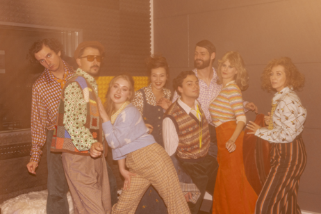 Grupa aktorów i aktorek przebranych w kolorowe stroje w stylu lat 80.